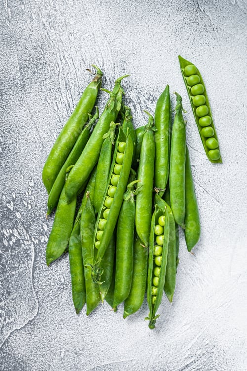 Preview: Peas and green pea pods on a kitchen table. White background. Top view
