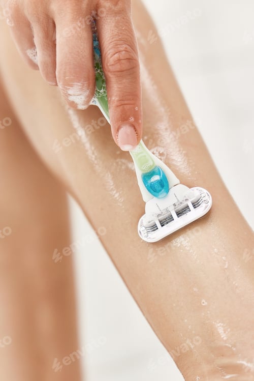 Preview: Young woman shaving her legs in white shower
