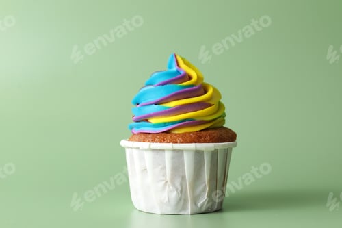 Preview: Tasty cupcake with colorful cream on light green background, closeup