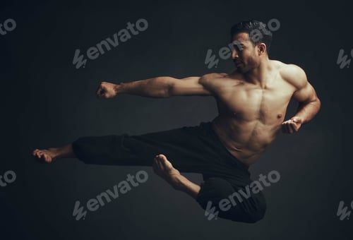 Preview: Full length shot of an unrecognisable man performing a martial arts kick in the studio