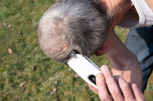 Preview: middle-aged man with gray hair cuts his hair with an electric hair clipper,beauty treatments for men