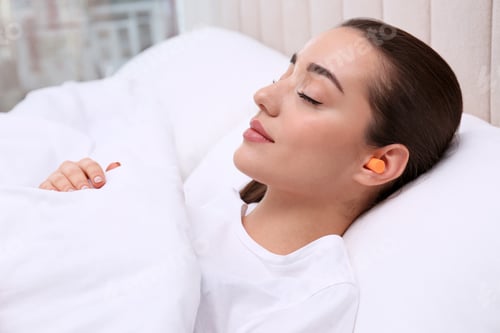 Preview: Young woman with foam ear plugs sleeping in bed