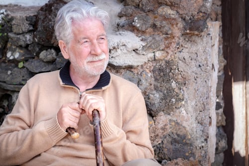 Preview: Portrait of beautiful senior man sitting outdoors against a stone wall.