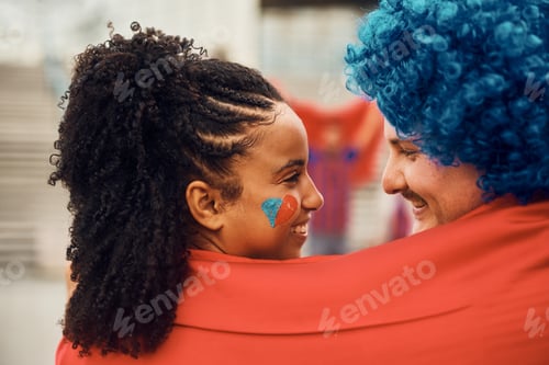 Preview: Loving couple of sports fans wrapped in favorite team's flag looking at each other.
