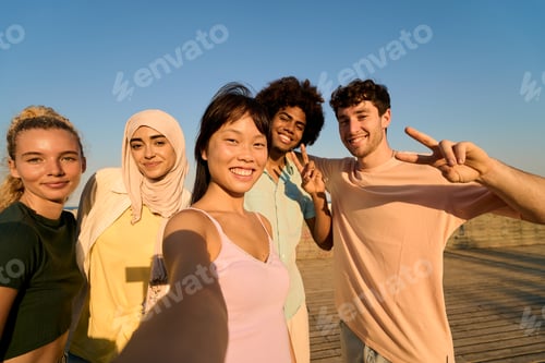 Preview: Happy multi ethnic friends taking selfie outdoors showing peace sign
