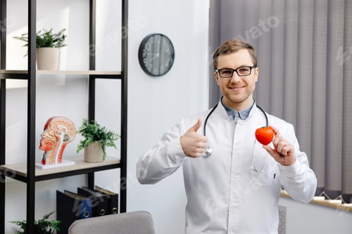 Preview: Doctor in white coat and glasses holding a red heart at hospital office