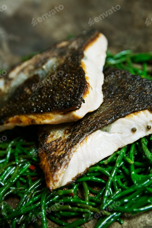 Preview: Close up of grilled fish fillets with crispy skin on a bed of samphire.