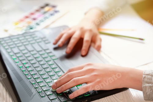 Preview: The laptop keyboard is black. Beautiful hands on laptop keys near paints and pencils. Online drawing