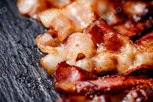 Preview: Strips of fried bacon on a black background.