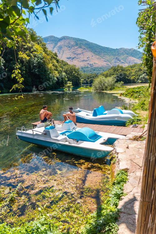 Preview: Two men sitting next to some pedalos in the river of The Blue Eye or Syri i kalter