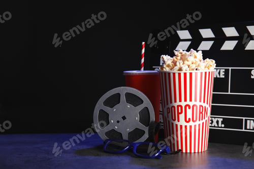 Vorschau: Schindel, Rolle und Popcorn auf dem Tisch vor dunklem Hintergrund, Platz für Text. Kino schauen