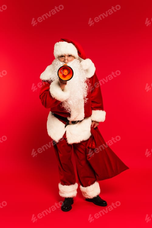 Preview: Father christmas in costume holding sack and loudspeaker on red background