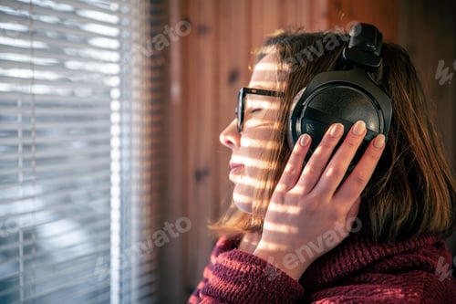 Preview: A woman with headphones looks through the blinds at the early morning sunlight.
