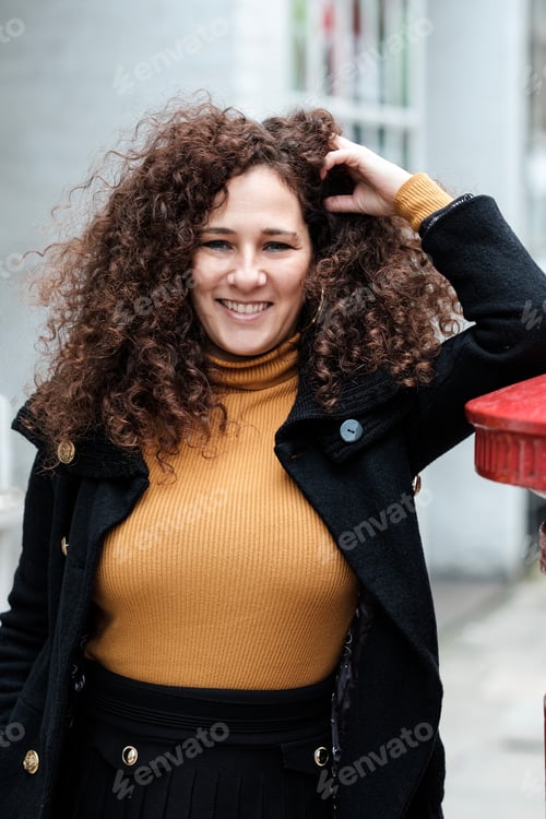 Preview: Relaxed and fun mature curly woman leaning on postbox in the street.
