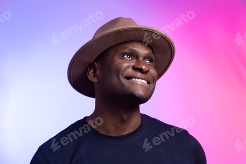 Preview: Smiling happy american african man wear stylish hat on pink and purple background. Festive and party