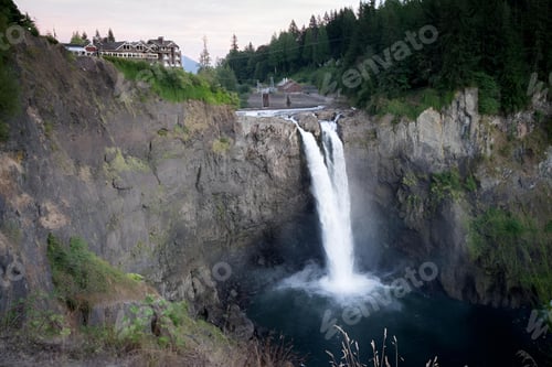 Preview: waterfall flowing over a cliff in front of hotel buildings in the mountains