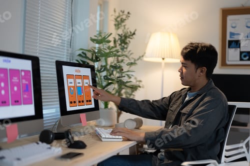 Preview: Ui designer is working late, reviewing the design of a mobile app on his computer. He is pointing at
