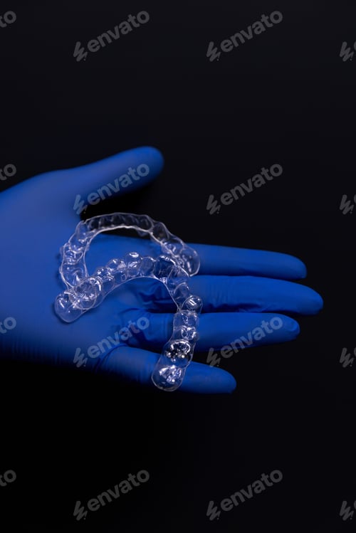 Preview: A dentist in blue rubber gloves holds transparent plastic aligners