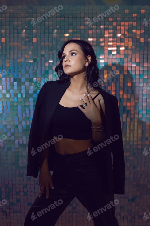 Preview: exy young energetic woman in black suit in the studio against a background of shiny squares