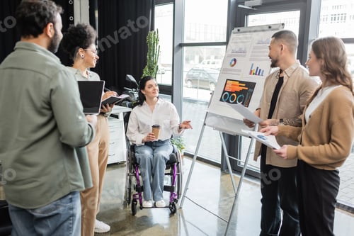 Preview: inclusion concept, disabled woman in wheelchair sharing ideas with interracial startup team