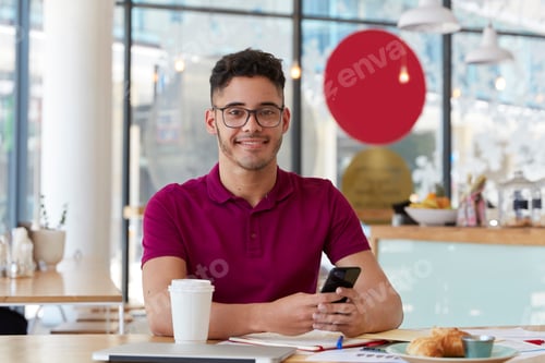Preview: Handsome cheerful young man searches job, browses webpage on modern cell phone, checks information i