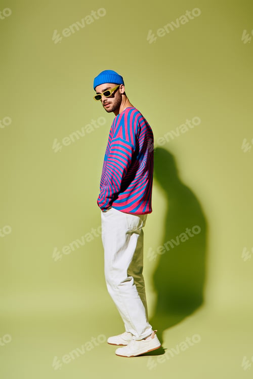 Preview: Handsome young man flaunts modern style in vibrant outfit against bright green backdrop