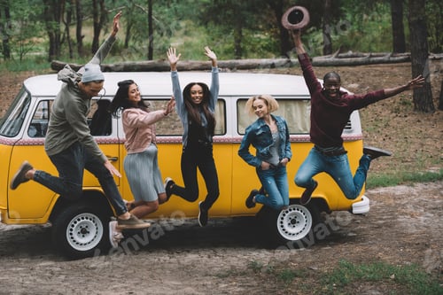 Preview: young multiethnic friends jumping and having fun together at retro minivan in forest