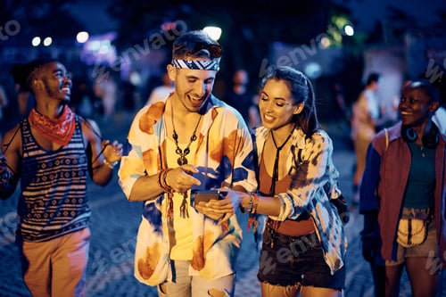 Preview: Happy couple using cell phone on summer music concert at night.