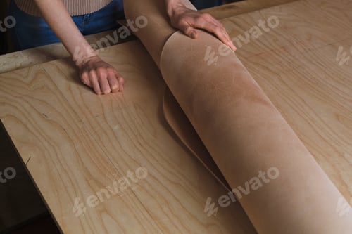 Preview: experienced female leather craftsman proudly presenting a roll of luxurious leather, illustrating