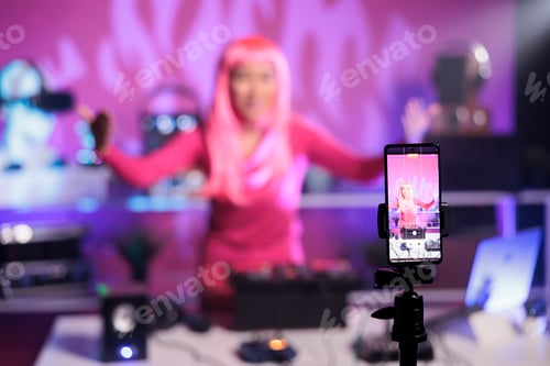 Preview: Woman with pink hair standing at dj table mixing song with turntables in front of camera