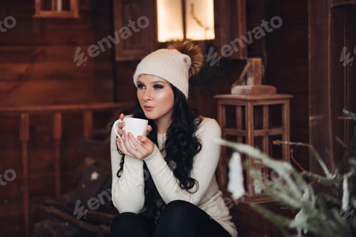 Preview: Romantic brunette girl in hat drinking hot cacao under snowfall