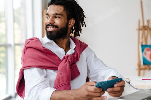 Preview: Joyful african american guy smiling and playing video game on cellphone
