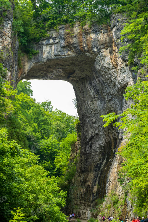 Preview: Beautiful Natural Bridge in Virginia covered by green lush trees and a group of visitors below