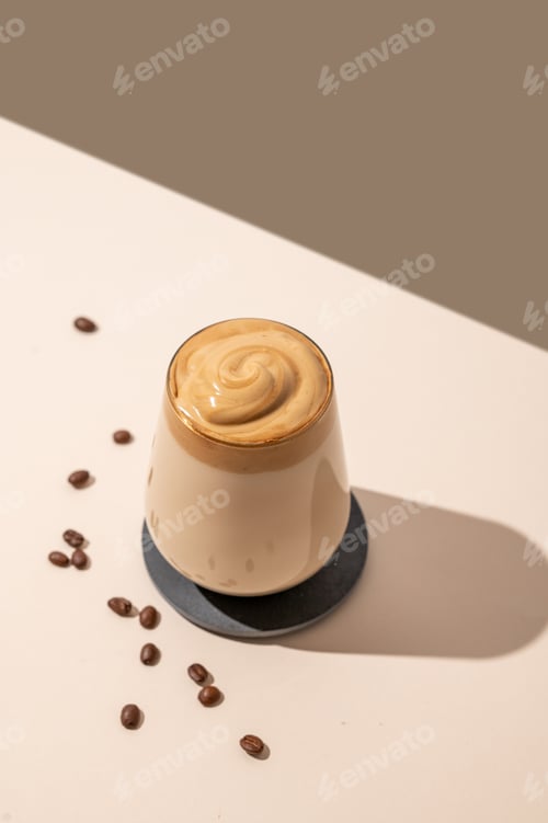 Preview: Dalgona coffee. Whipped instant coffee in a glass with beans and shadow on a yellow background.