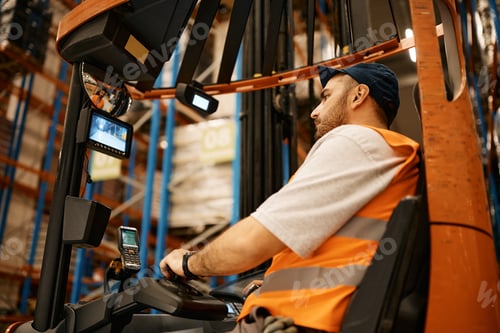 Preview: Young man driving forklift while working at storage compartment of distribution warehouse.