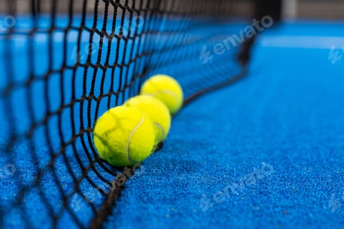 Preview: several balls by the net on a blue paddle tennis court