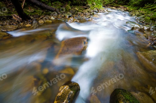 Preview: Fast flowing through wild green forest river with crystal clear smooth silky water falling from big