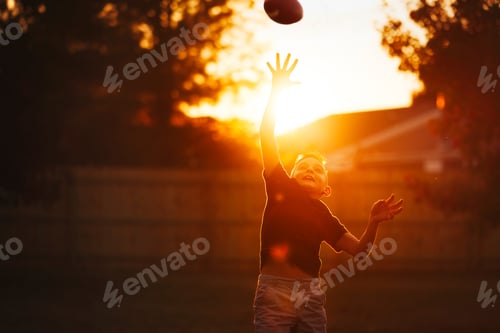 Preview: A joyful child catching a football during a vibrant sunset.