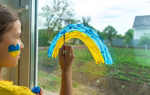 Preview: Children on the window painted a rainbow Ukraine peaceful sky. Selective focus.