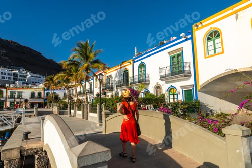 Preview: A tourist woman in a red dress on a bridge in the port of the town Mogan in Gran Canaria. Spain
