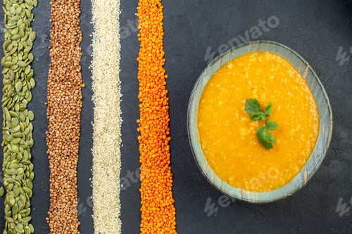 Preview: Top view of delicious soup in a bowl and assorted grains of buckwheat pumpkin seeds corns rice on