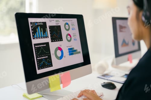 Preview: Businesswoman works on a financial report with graphs on a computer, wearing a headset for discussio