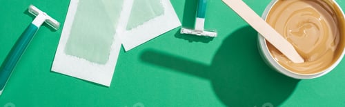 Preview: top view of green disposable razors, wax and depilation stripes on green background, panoramic shot