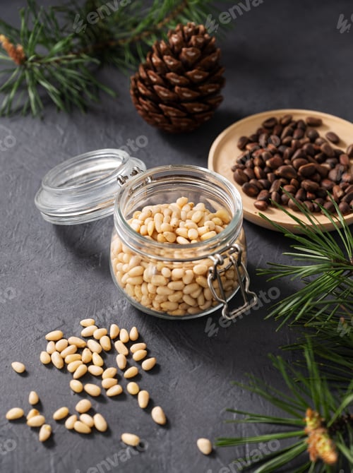Preview: Pine nuts in a jar, bowl and a scattered on a dark background with branches of pine needles and cone