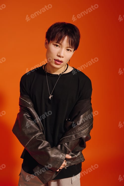 Preview: Stylish young asian man posing confidently against a vibrant orange background in casual wear