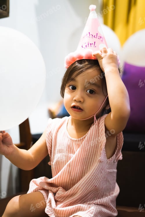 Preview: cute toddler girl wearing birthday hat holding balloons