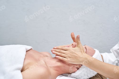 Preview: Female receiving facial massage at spa by professional therapist in relaxing setting