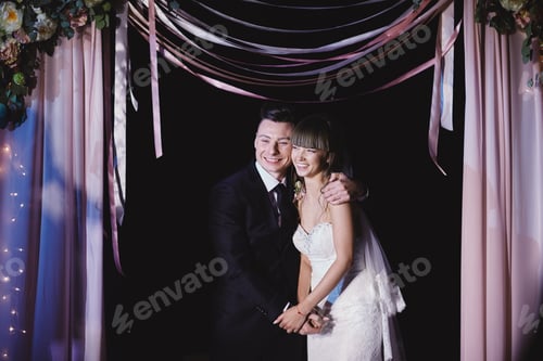 Preview: Fashionable newlyweds stand at night against the backdrop of chic decorations and flowers,electric