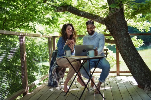 Preview: Happy couple with laptop resting outdoors in a tree house, weekend away and remote office concept.