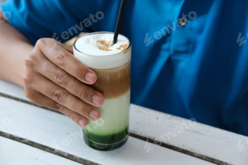 Preview: A hand holding a refreshing layered iced drink consisting of green tea, milk, and coffee